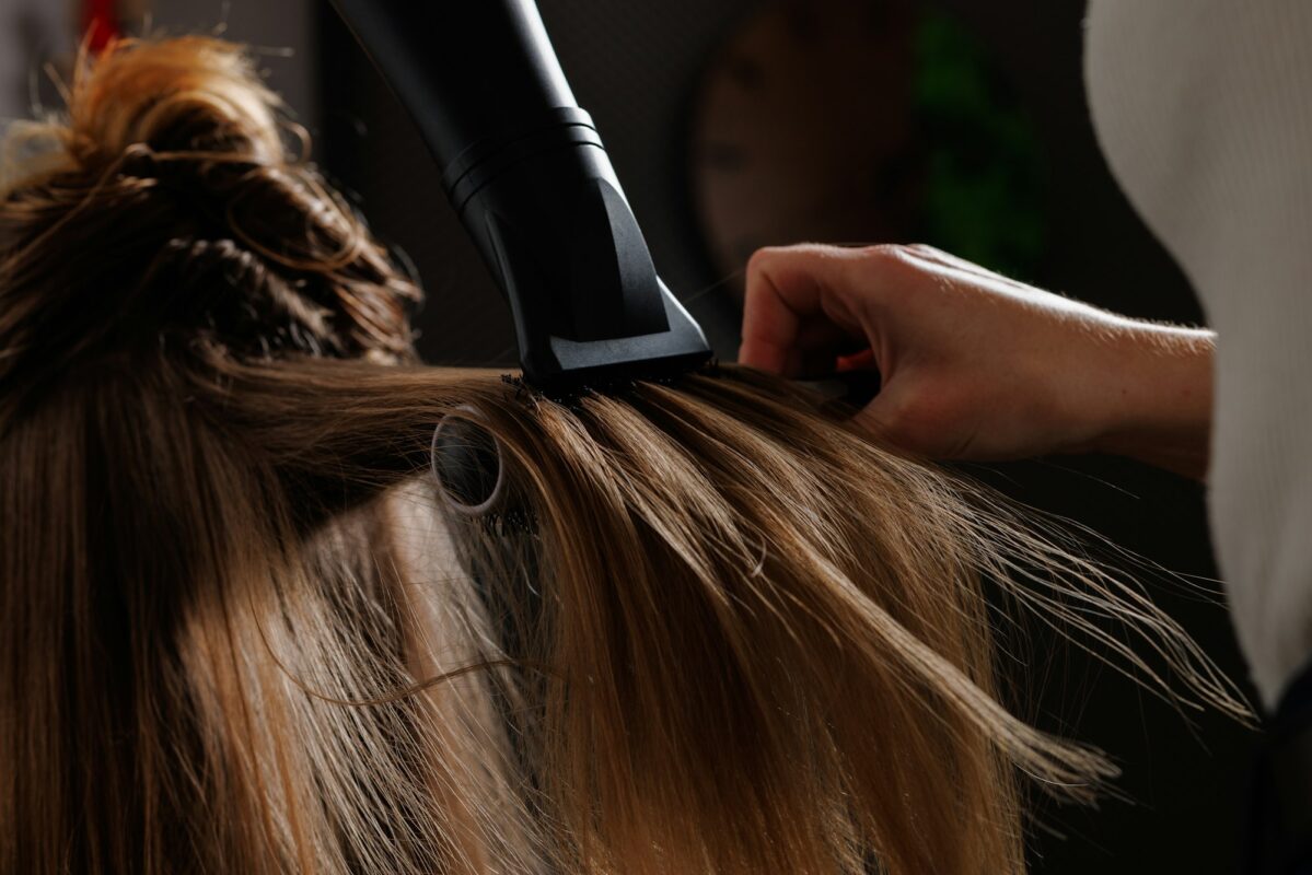hairdresser drying hair with hair dryer and comb in beauty salon, drying hair close-up